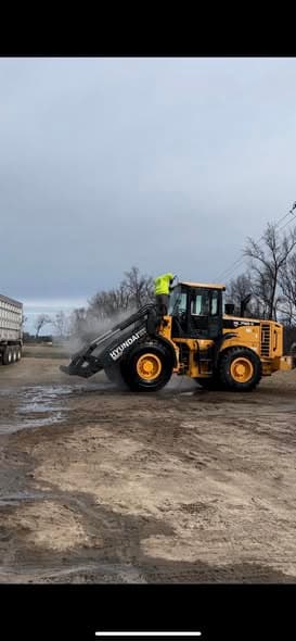 A wheel loader being rinsed down in a dusty commercial yard.